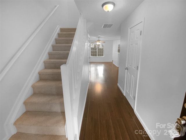 staircase with a ceiling fan, visible vents, baseboards, and wood finished floors