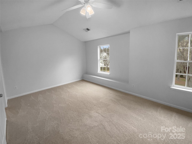 carpeted empty room featuring lofted ceiling, baseboards, visible vents, and a wealth of natural light