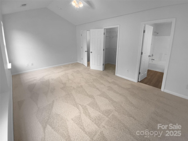 unfurnished bedroom featuring carpet floors, a walk in closet, visible vents, vaulted ceiling, and baseboards