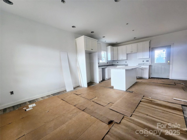 kitchen featuring baseboards, light countertops, white cabinetry, and a center island