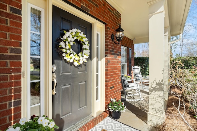 view of exterior entry with brick siding and a porch