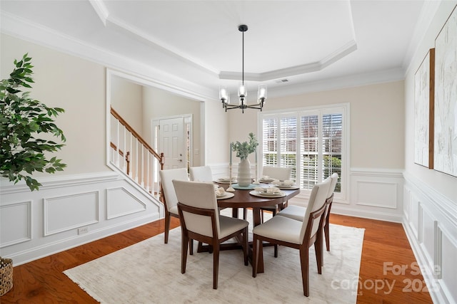 dining space featuring visible vents, a notable chandelier, a tray ceiling, light wood finished floors, and stairs