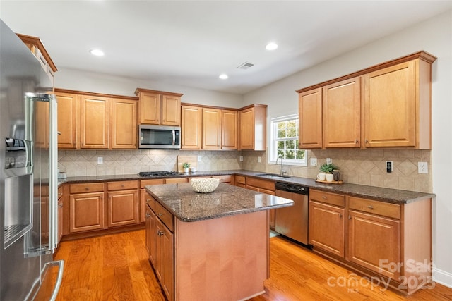 kitchen with visible vents, a kitchen island, light wood-type flooring, appliances with stainless steel finishes, and a sink