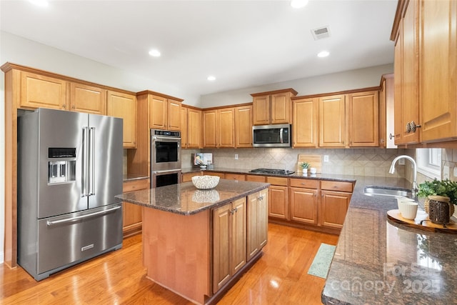 kitchen with visible vents, a center island, dark stone countertops, appliances with stainless steel finishes, and a sink