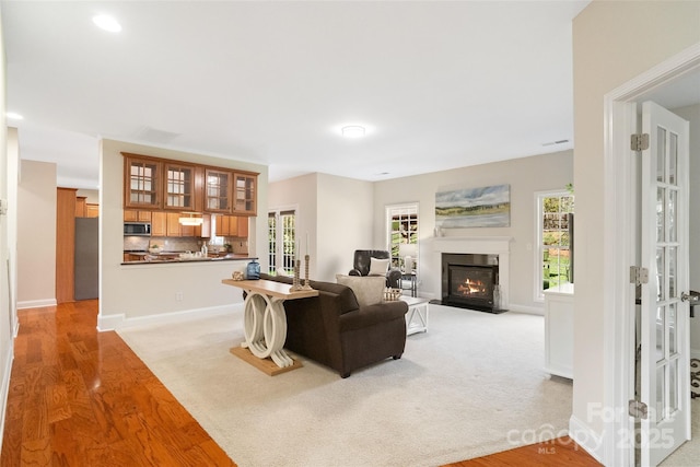 living room featuring baseboards, a fireplace with flush hearth, light wood-style floors, and visible vents