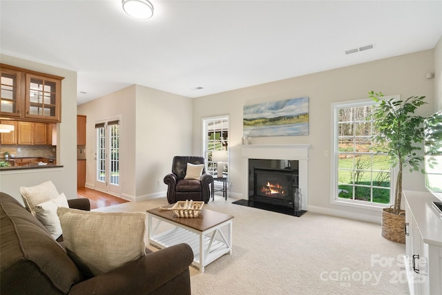 living area featuring light carpet, visible vents, baseboards, and a fireplace with flush hearth