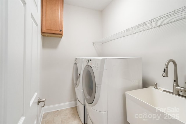 clothes washing area featuring a sink, baseboards, cabinet space, and separate washer and dryer