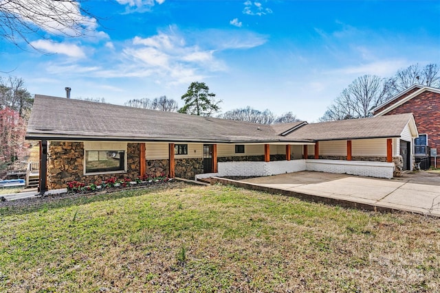 view of front of home with stone siding, roof with shingles, a front lawn, and a patio