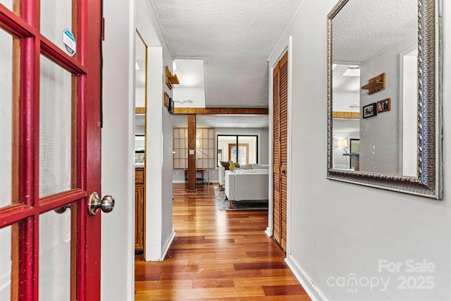 hall with a textured ceiling, baseboards, and wood finished floors