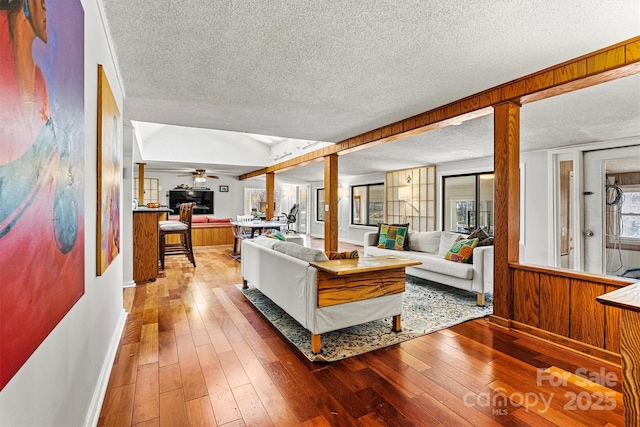 living room featuring wooden walls, ceiling fan, a textured ceiling, and hardwood / wood-style floors