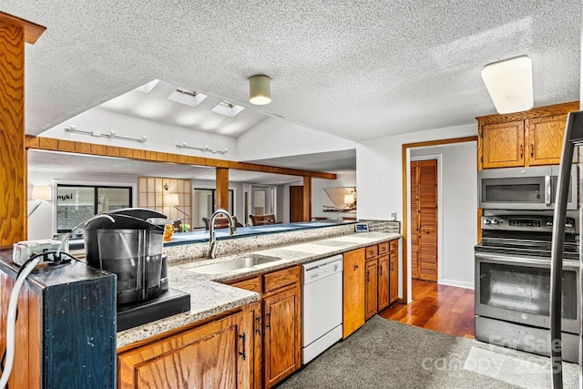 kitchen with light stone counters, a sink, appliances with stainless steel finishes, brown cabinets, and dark wood finished floors