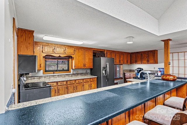 kitchen with decorative columns, brown cabinetry, fridge with ice dispenser, a textured ceiling, and black electric range