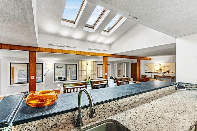 kitchen featuring a skylight, a sink, a textured ceiling, high vaulted ceiling, and baseboards