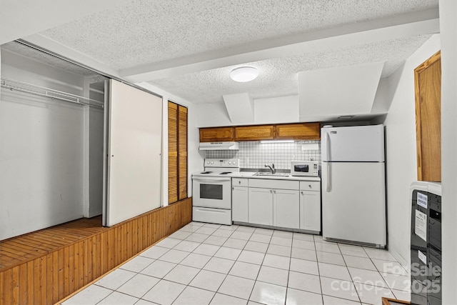 kitchen with light tile patterned flooring, under cabinet range hood, white appliances, a sink, and tasteful backsplash