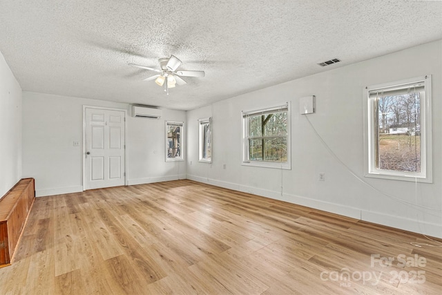 empty room with light wood finished floors, baseboards, visible vents, and a wall mounted air conditioner