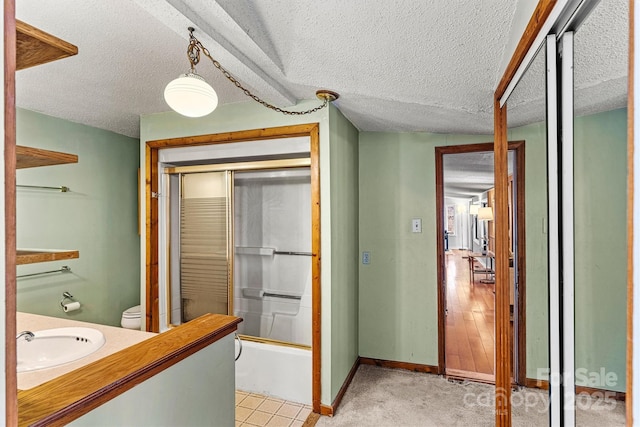 bathroom featuring toilet, a textured ceiling, vanity, and bath / shower combo with glass door