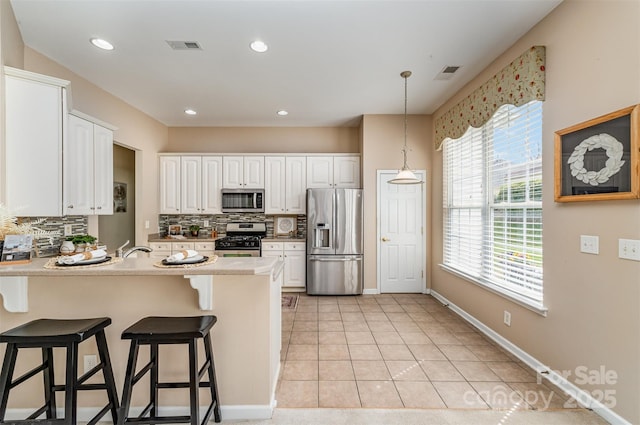 kitchen featuring visible vents, a breakfast bar, a peninsula, stainless steel appliances, and backsplash