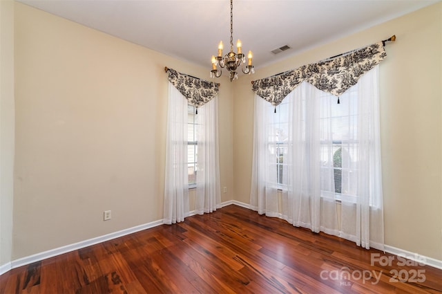 empty room with dark wood-type flooring, a notable chandelier, baseboards, and visible vents