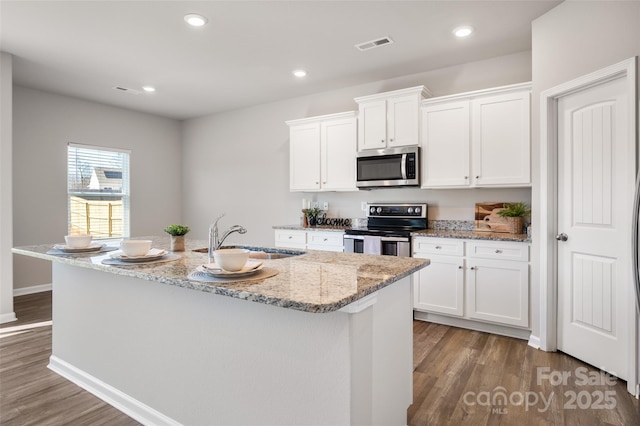 kitchen featuring stainless steel appliances, visible vents, white cabinetry, a sink, and wood finished floors