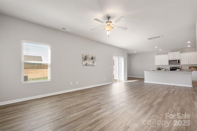 unfurnished living room featuring a ceiling fan, light wood-style flooring, visible vents, and baseboards