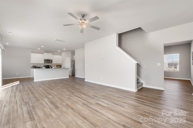 unfurnished living room featuring stairs, ceiling fan, light wood-style flooring, and baseboards