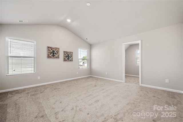 carpeted spare room with baseboards, visible vents, and vaulted ceiling