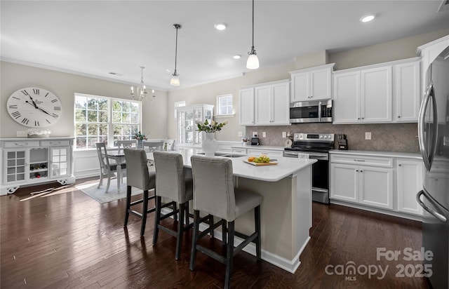 kitchen with tasteful backsplash, white cabinets, dark wood-type flooring, stainless steel appliances, and light countertops