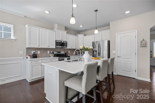 kitchen with a breakfast bar, a sink, white cabinetry, appliances with stainless steel finishes, and decorative backsplash