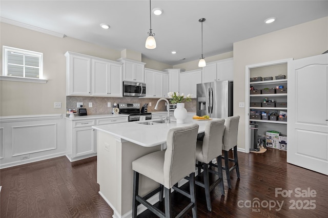 kitchen featuring a sink, a kitchen breakfast bar, light countertops, appliances with stainless steel finishes, and dark wood finished floors