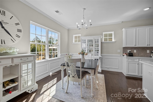 dining space with visible vents, dark wood finished floors, a wainscoted wall, ornamental molding, and a chandelier