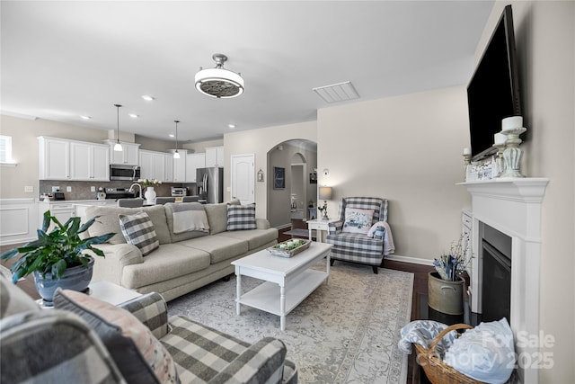 living area with arched walkways, recessed lighting, visible vents, light wood finished floors, and a glass covered fireplace