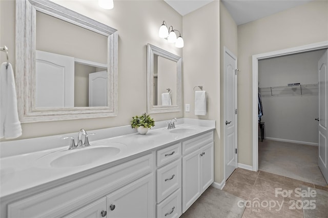 bathroom with double vanity, a sink, a walk in closet, and tile patterned floors