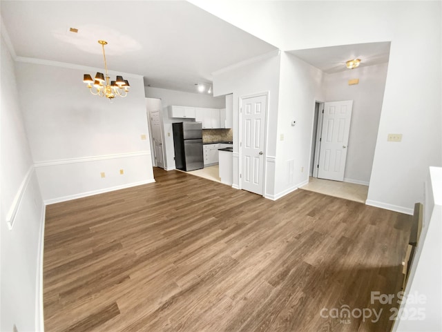 unfurnished living room with a chandelier, ornamental molding, wood finished floors, and baseboards