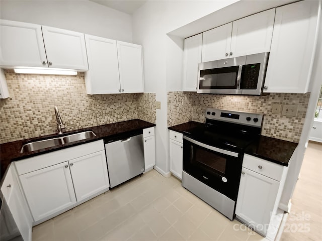 kitchen with tasteful backsplash, dark countertops, appliances with stainless steel finishes, white cabinetry, and a sink