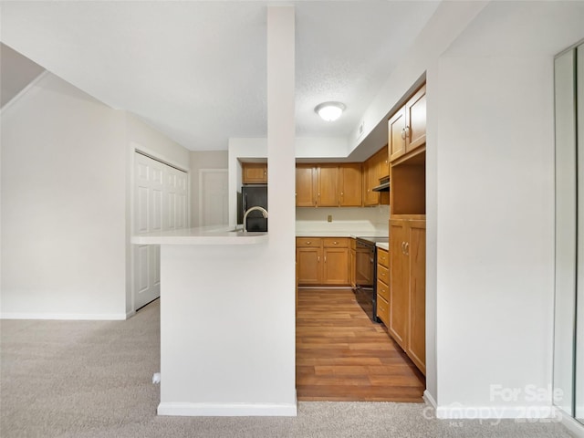 kitchen featuring light countertops, light colored carpet, a peninsula, under cabinet range hood, and black appliances