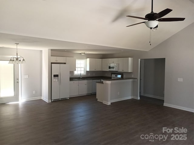 kitchen featuring a peninsula, white appliances, white cabinetry, dark countertops, and dark wood finished floors