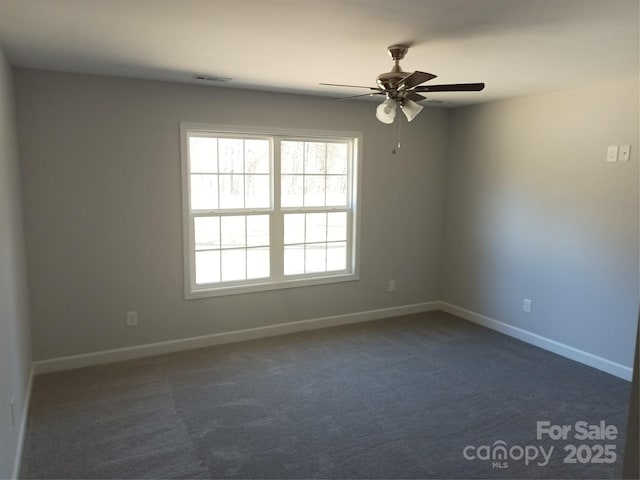 spare room with a wealth of natural light, baseboards, and dark colored carpet