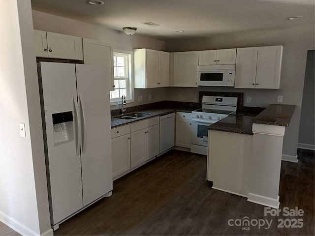 kitchen featuring a peninsula, white appliances, dark wood-style flooring, a sink, and white cabinetry