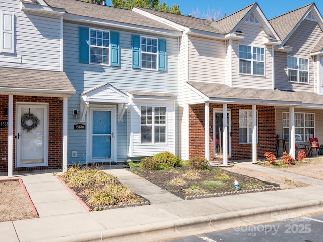 multi unit property with brick siding, roof with shingles, and a porch