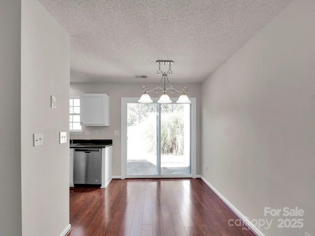 unfurnished dining area with dark wood-style flooring, visible vents, a textured ceiling, and baseboards