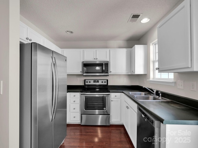 kitchen featuring stainless steel appliances, dark countertops, visible vents, and a sink