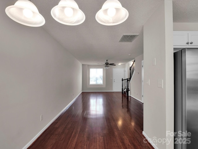 unfurnished living room featuring visible vents, a textured ceiling, wood finished floors, baseboards, and stairs