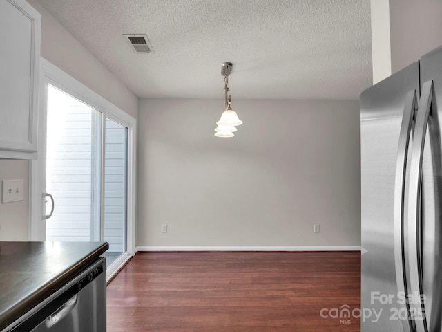 unfurnished dining area featuring dark wood-type flooring, visible vents, a textured ceiling, and baseboards