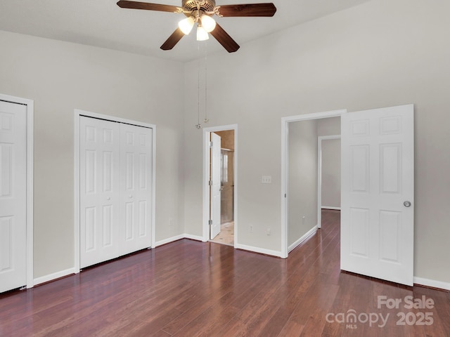 unfurnished bedroom featuring multiple closets, a towering ceiling, baseboards, and wood finished floors