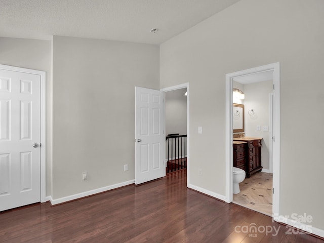 unfurnished bedroom featuring a textured ceiling, connected bathroom, wood finished floors, baseboards, and vaulted ceiling