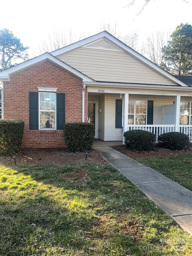 view of front of home with a porch, brick siding, and a front lawn