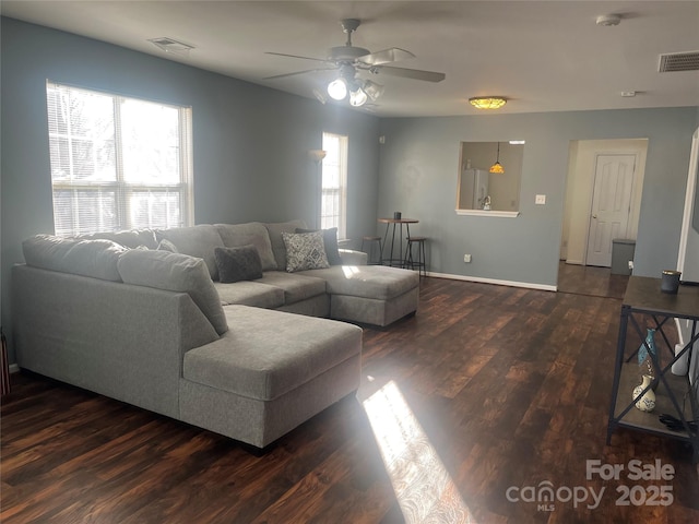 living room featuring dark wood-style floors, a ceiling fan, visible vents, and baseboards