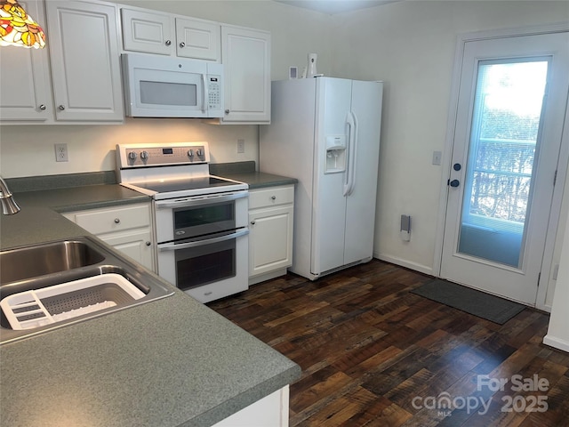 kitchen with white appliances, dark wood-style flooring, a sink, white cabinetry, and dark countertops