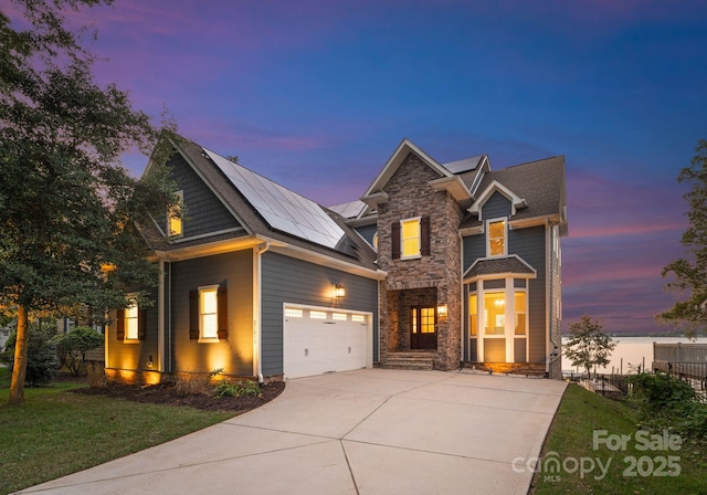 traditional-style home featuring driveway, stone siding, an attached garage, and solar panels