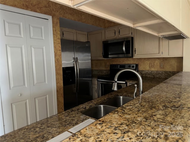 kitchen featuring appliances with stainless steel finishes, dark stone countertops, and a sink